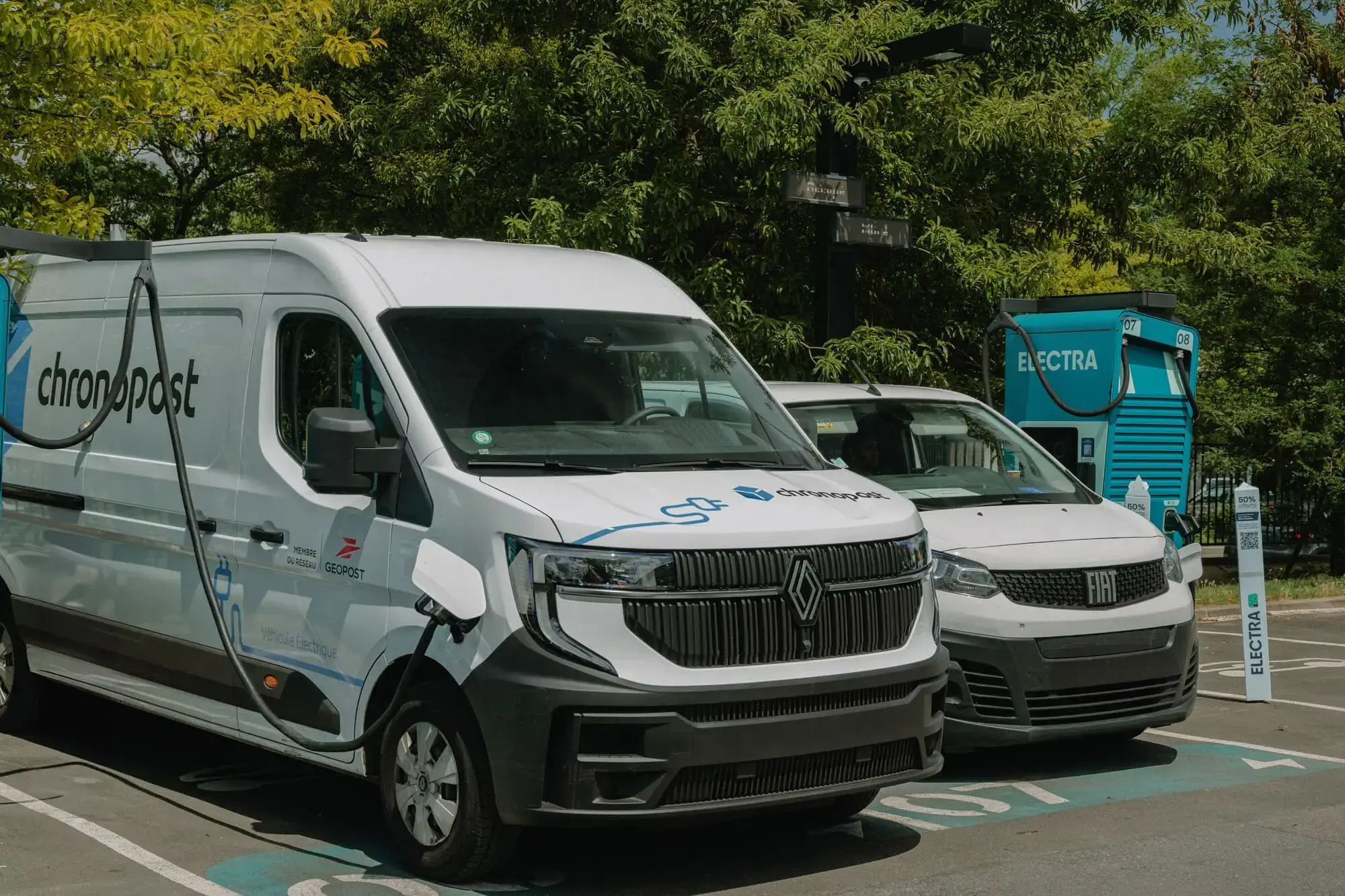 Two delivery vans parked at an Electra charging station, surrounded by trees. One van displays "chronopost" branding.