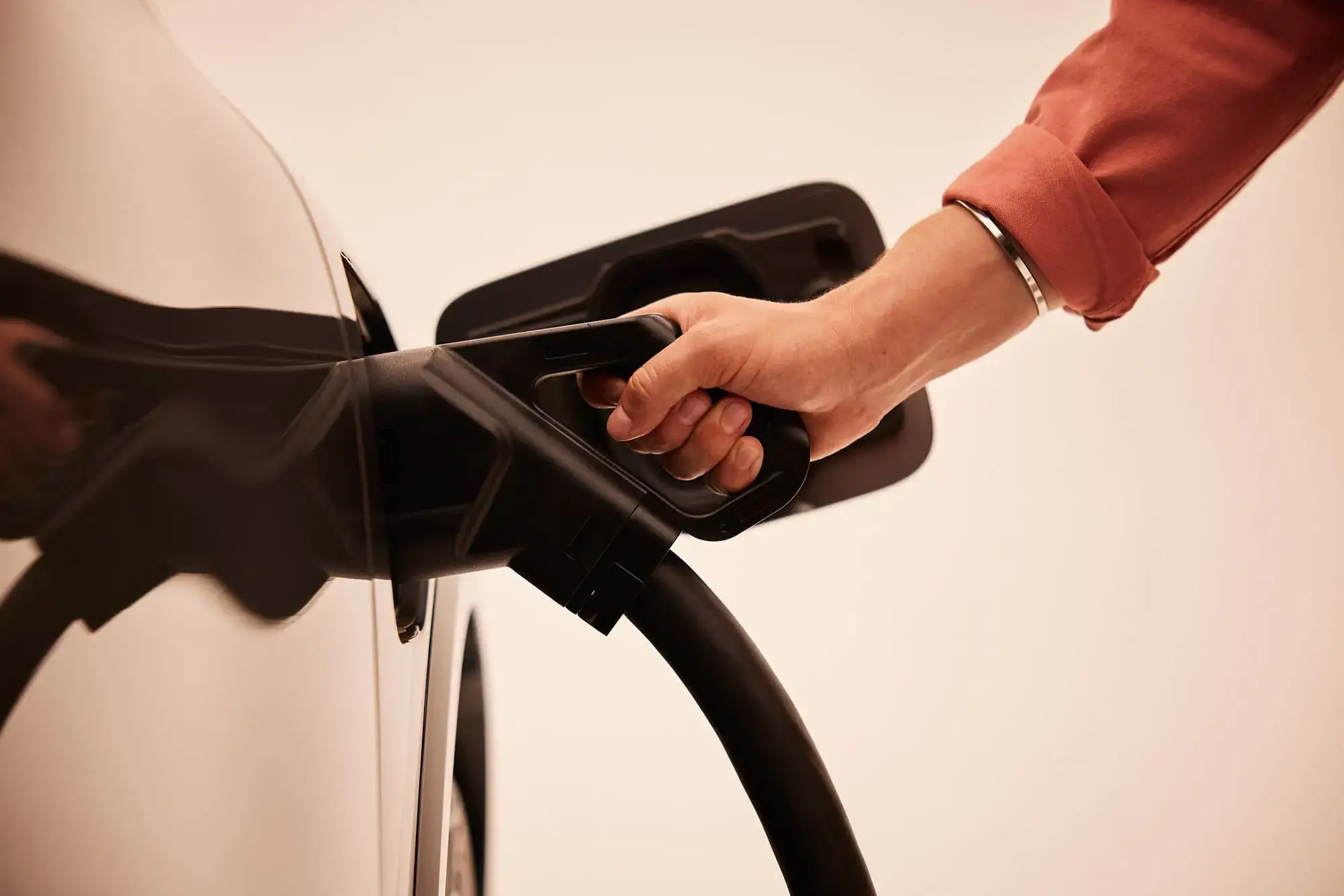 Person plugging a charging cable into an electric car, with a close-up of the hand and vehicle in a neutral background. Electra charging station