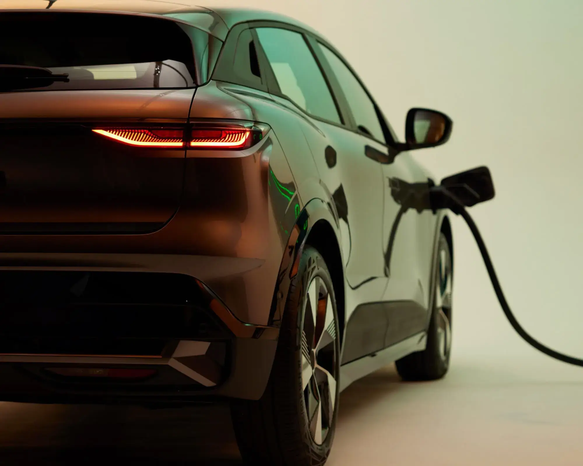 Electric car charging, rear view. The vehicle is plugged in an ELECTRA charging point, with taillights illuminated, set against a softly lit background.