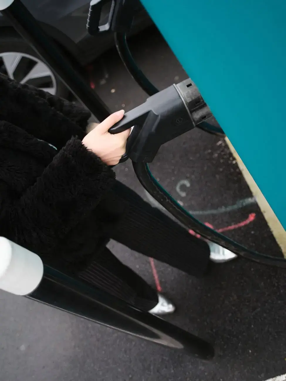 Person in classic clothing plugging a charging cable into an electric vehicle at an ELECTRA charging station.